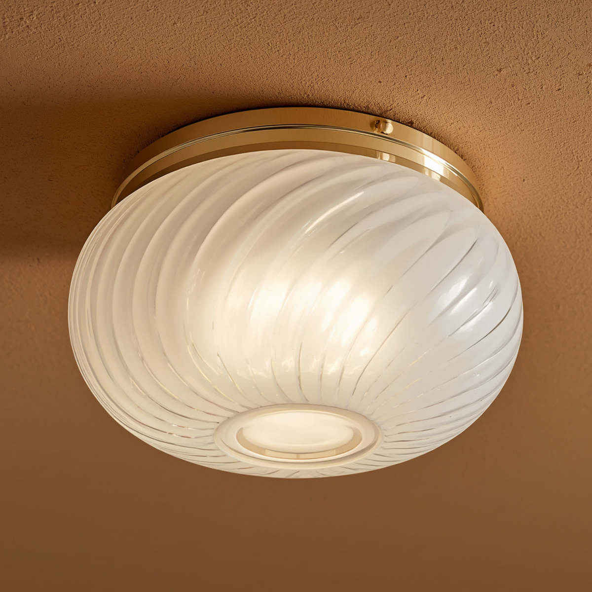 A flush mount ceiling light with a swirled frosted glass bowl and gold-tone metal trim mounted on a warm-toned ceiling.