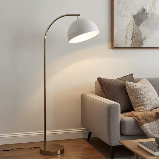 A gold arched floor lamp with a white dome shade standing next to a gray sofa in a living room.