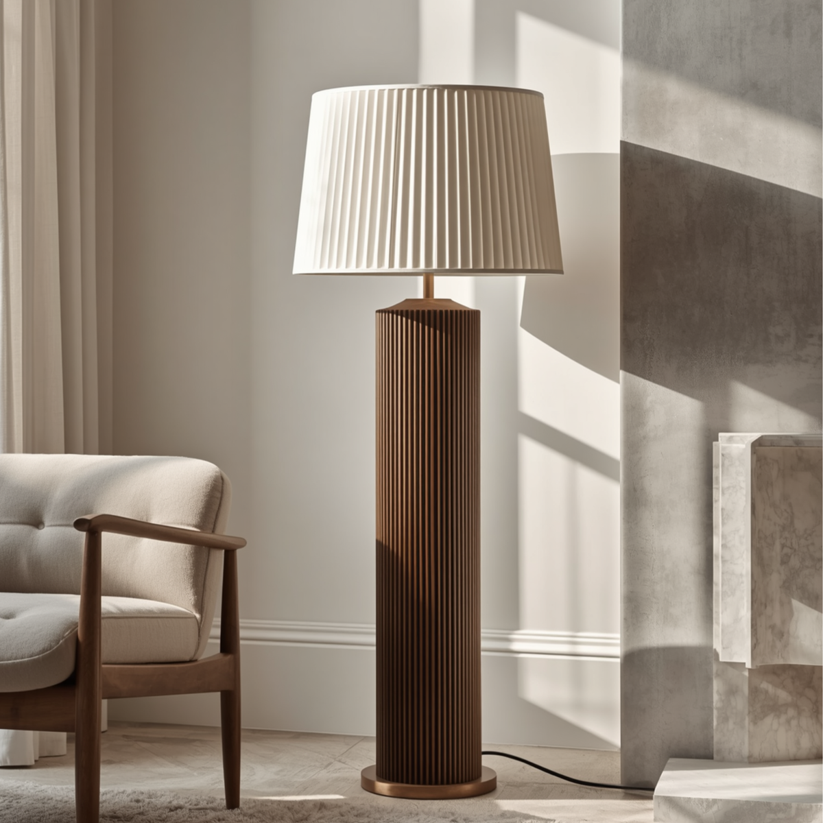 A fluted wooden pillar floor lamp with a pleated fabric shade standing next to an armchair and a fireplace in a bright room.