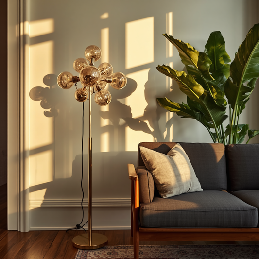 A gold-tone multi-bulb clustered branch floor lamp standing next to a gray sofa and a large potted plant on a wooden floor.  